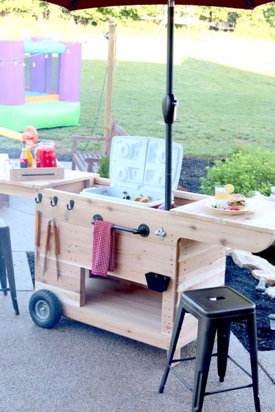 Outdoor party station mobile cart featuring storage for a large cooler, drawer that pulls out and doubles as a serving tray, pipe towel bar, and kiddie table! So COOL!