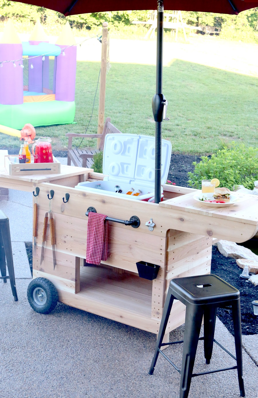 Outdoor party station mobile cart featuring storage for a large cooler, drawer that pulls out and doubles as a serving tray, pipe towel bar, and kiddie table! So COOL!